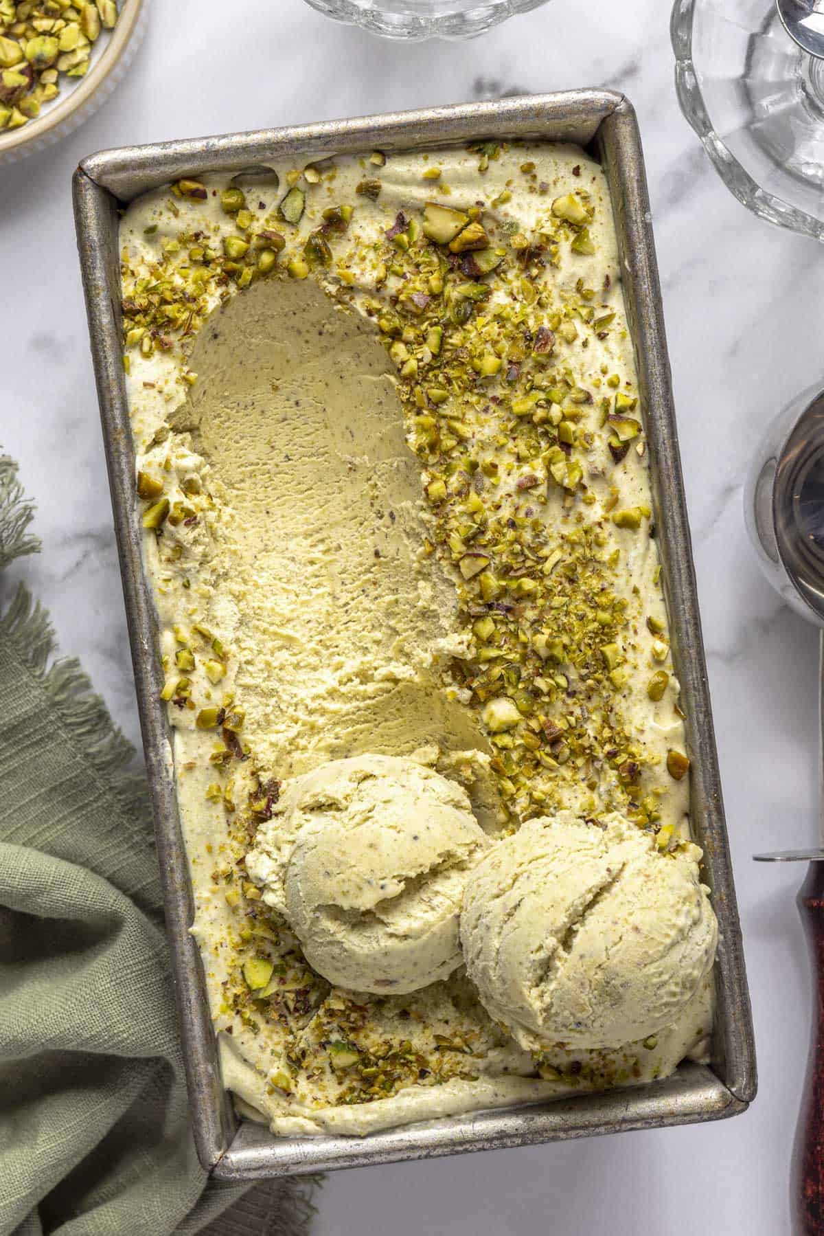 Easy pistachio ice cream recipe in a dish topped with chopped nuts and a few scoops of ice cream on top.