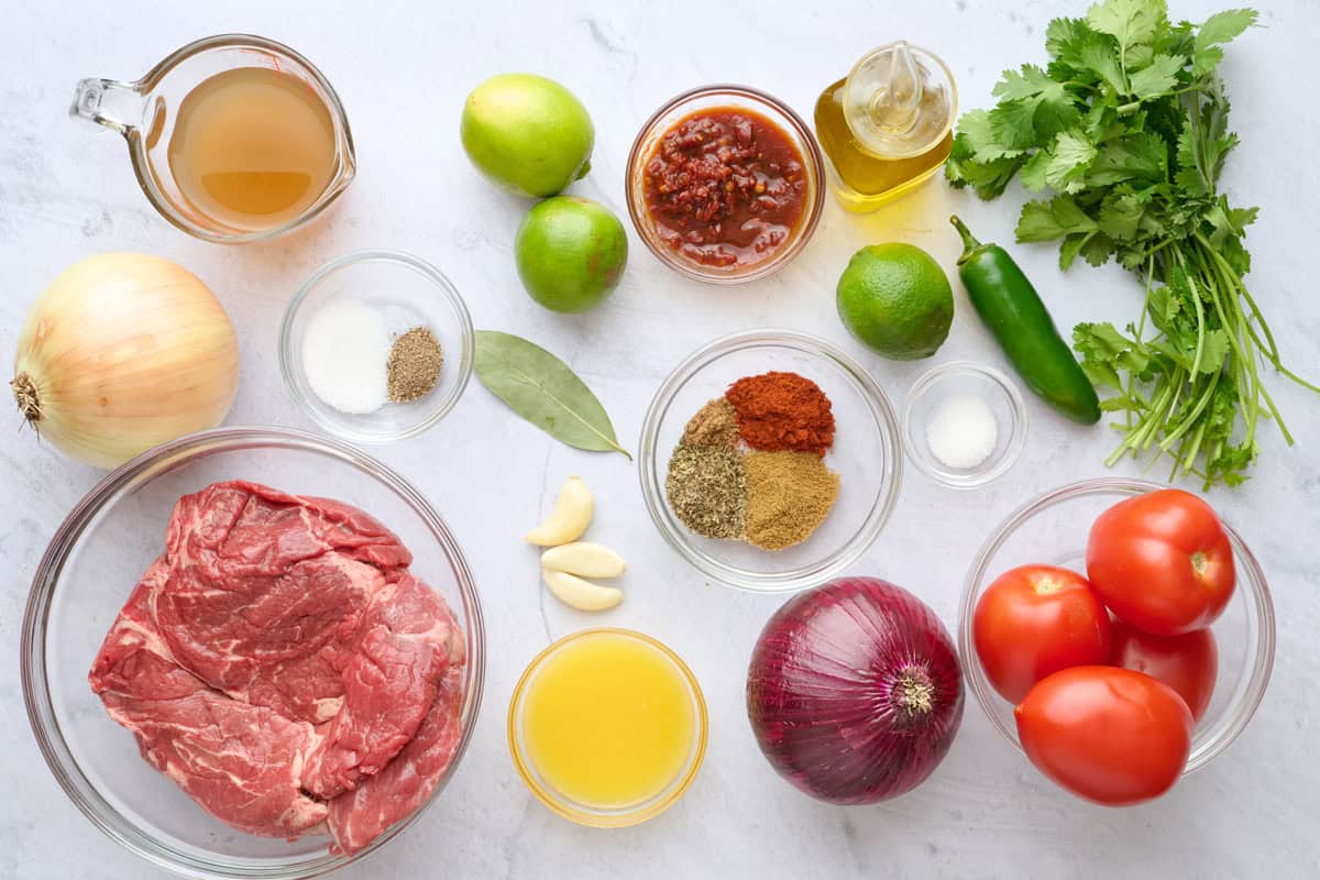 Ingredients for recipe: chuck roast, onion, broth, seasonings, garlic, chipotle peppers in adobe sauce, lime, oil, tomatoes, onions, cilantro, jalapeno, and orange juice.