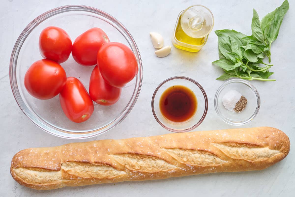 Ingredients for recipe: roma tomatoes, garlic, oil, basil, salt and pepper, balsamic vinegar, and a loaf of french baguette.