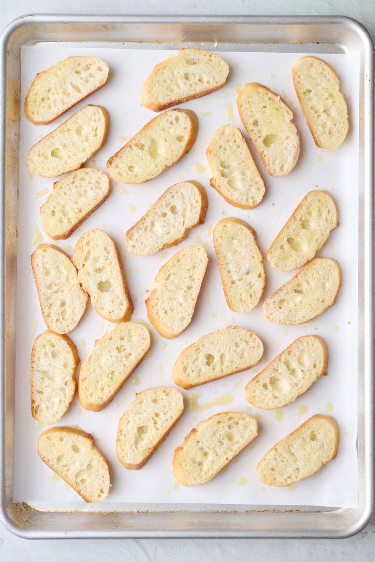 Bread slices on a baking sheet with oil drizzled on top.
