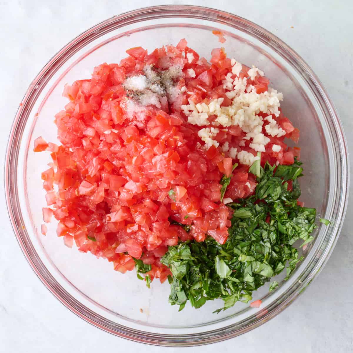 Diced tomatoes, garlic, chopped basil, oil, vinegar, and seasoning before tossing together in a bowl.
