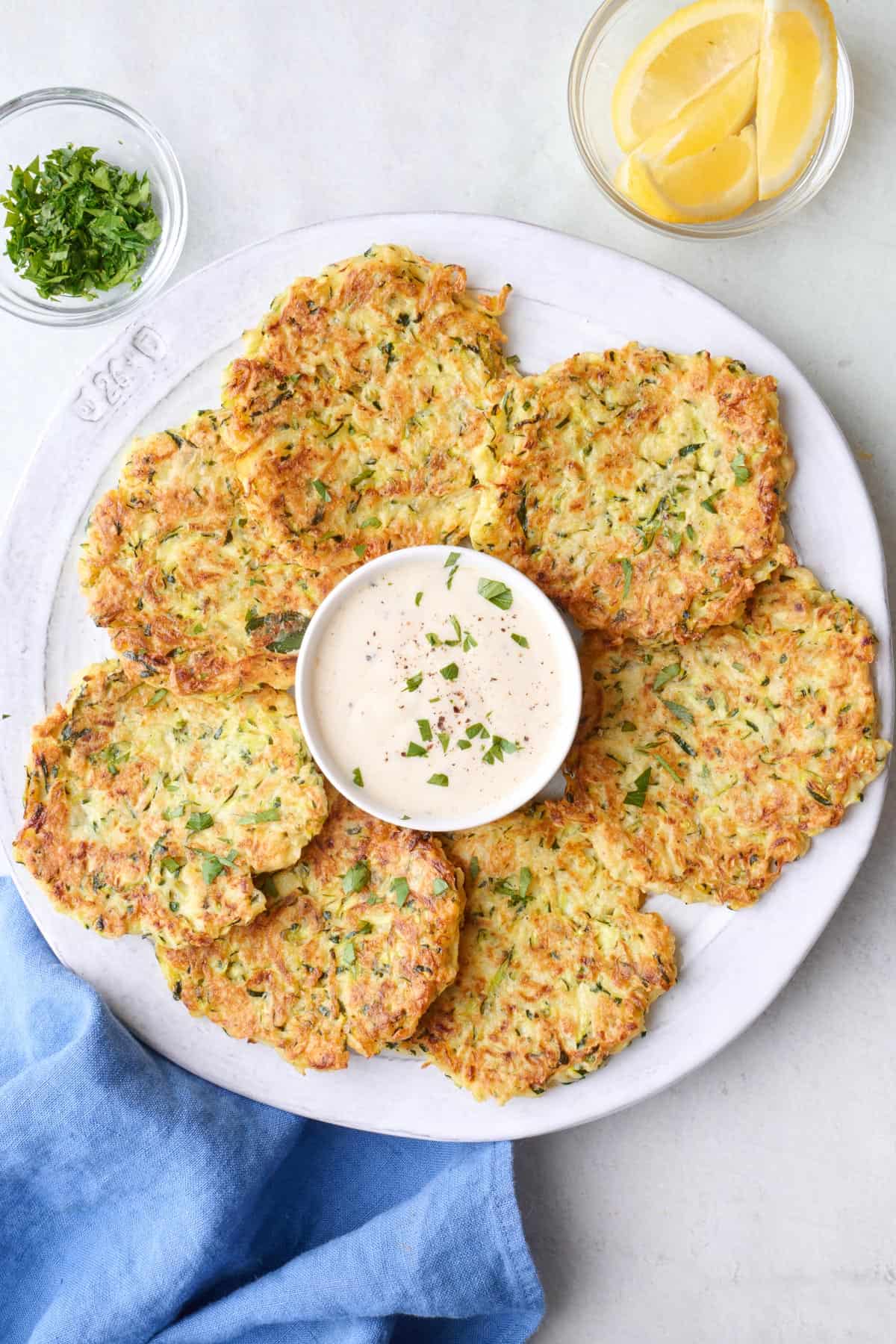 Zucchini fritters on a plate with a small dish of ranch dip in the center.