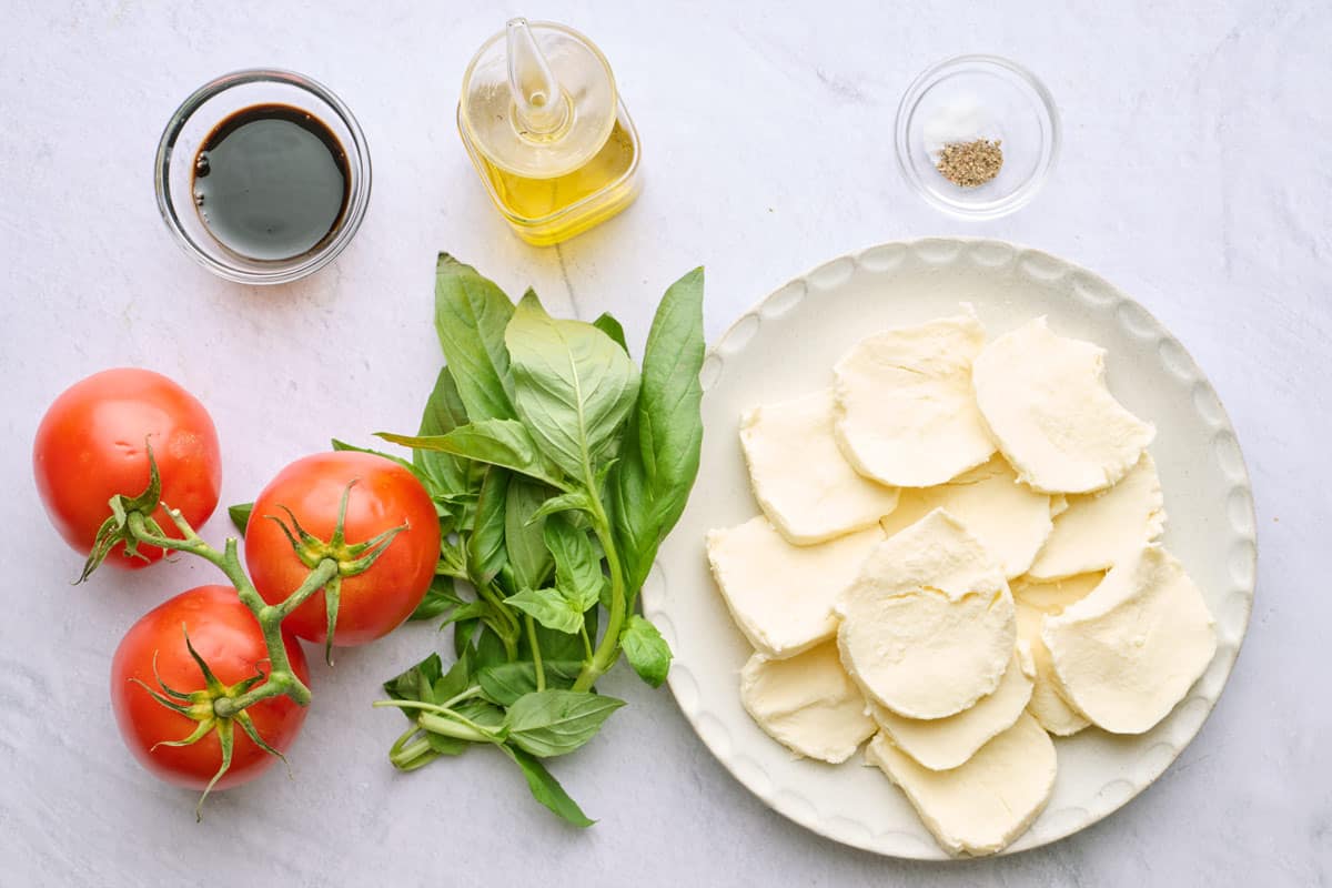 Ingredients for recipe: tomatoes, balsamic glaze, basil, oil, mozzarella slices, and seasonings.
