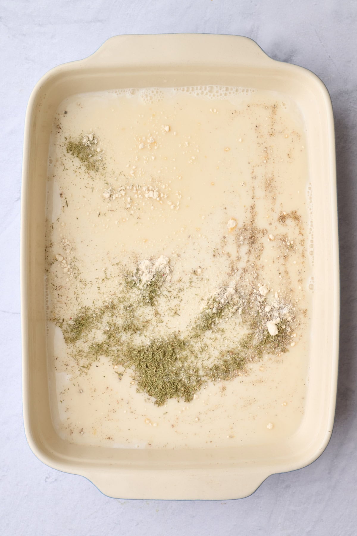 Broth, milk and seasonings in a casserole dish before whisking together.