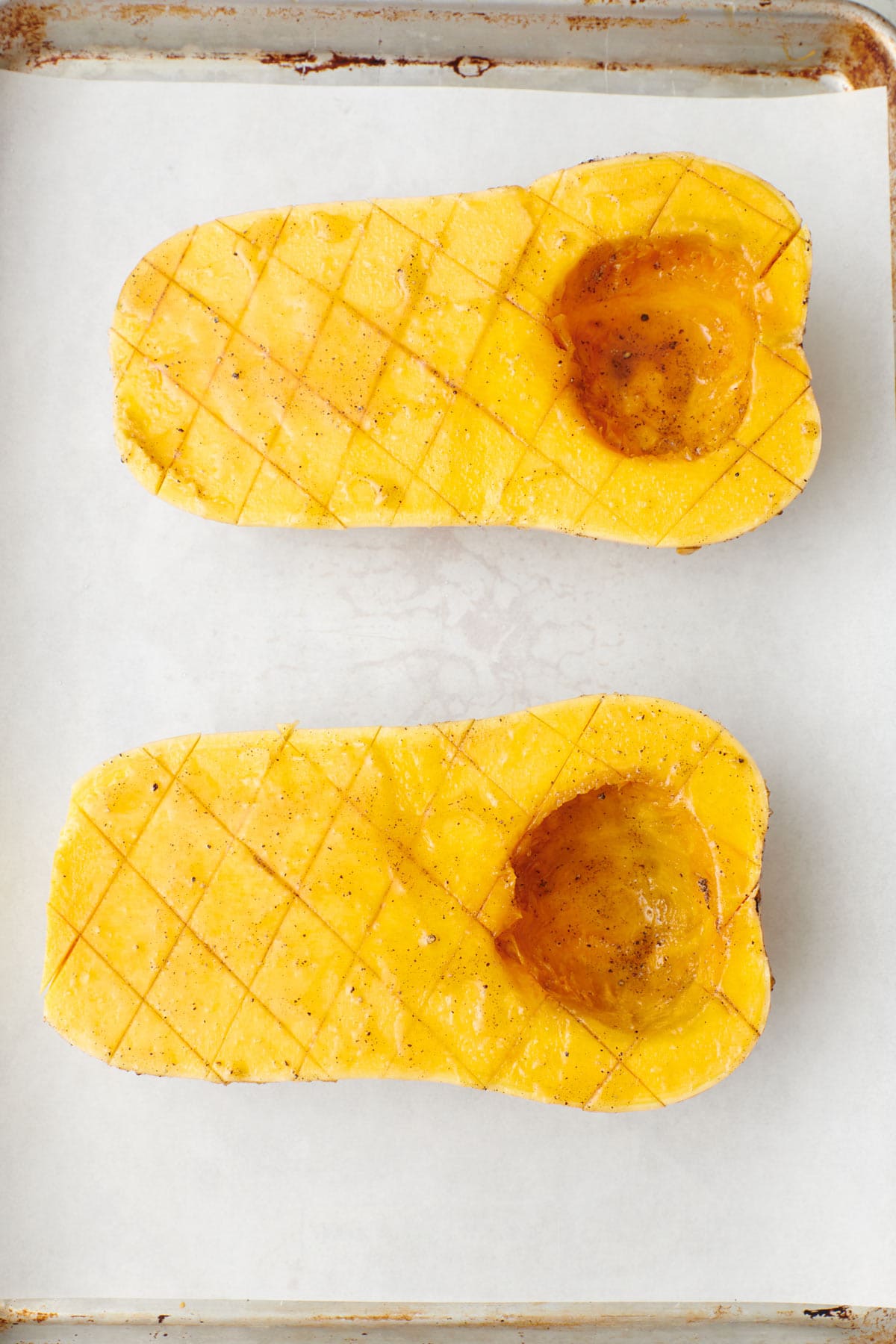 Squash halves on a parchment lined sheet pan before roasting, coated in oil and seasoning.