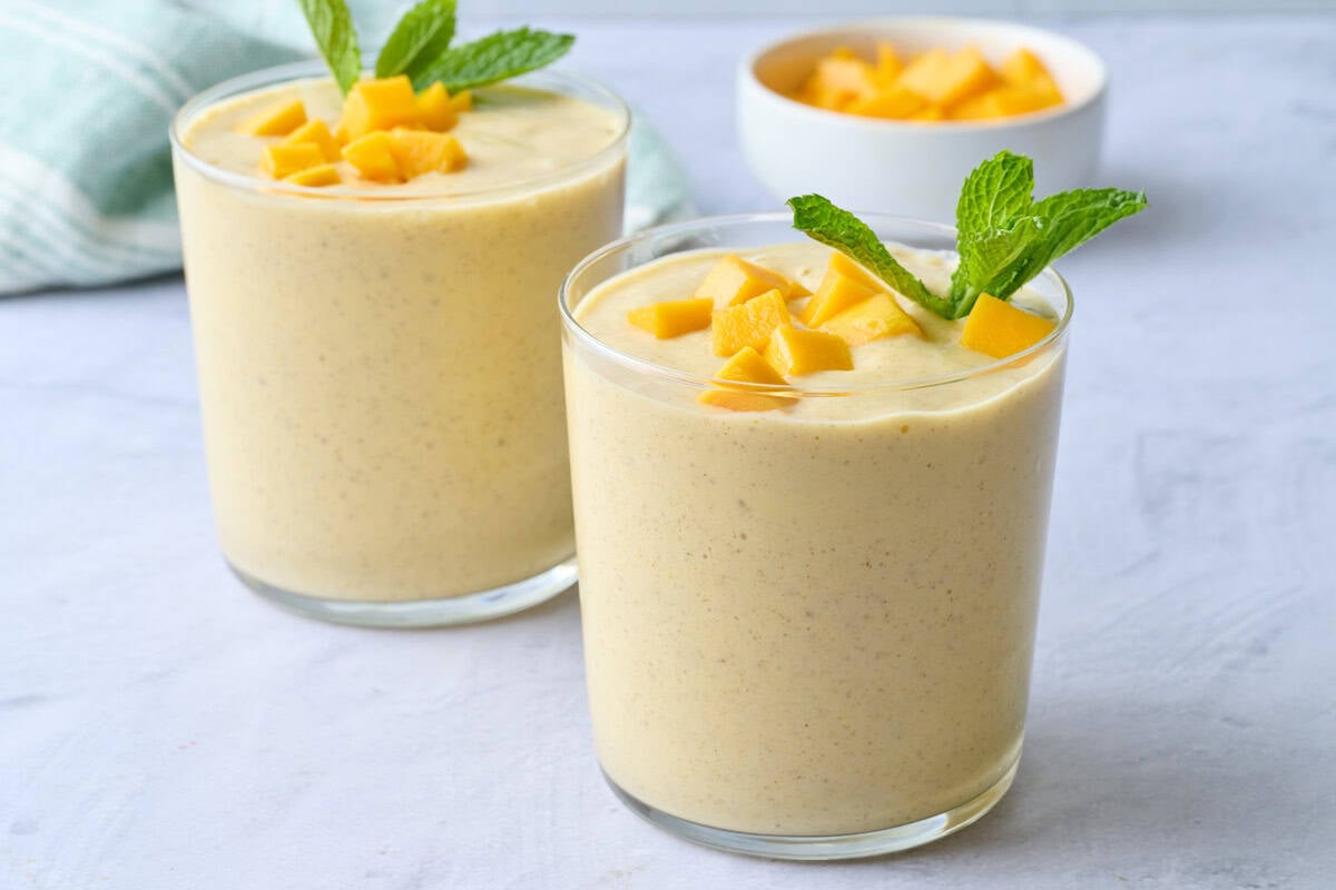 Easy mango smoothie in small glasses topped with extra diced mango and fresh mint.