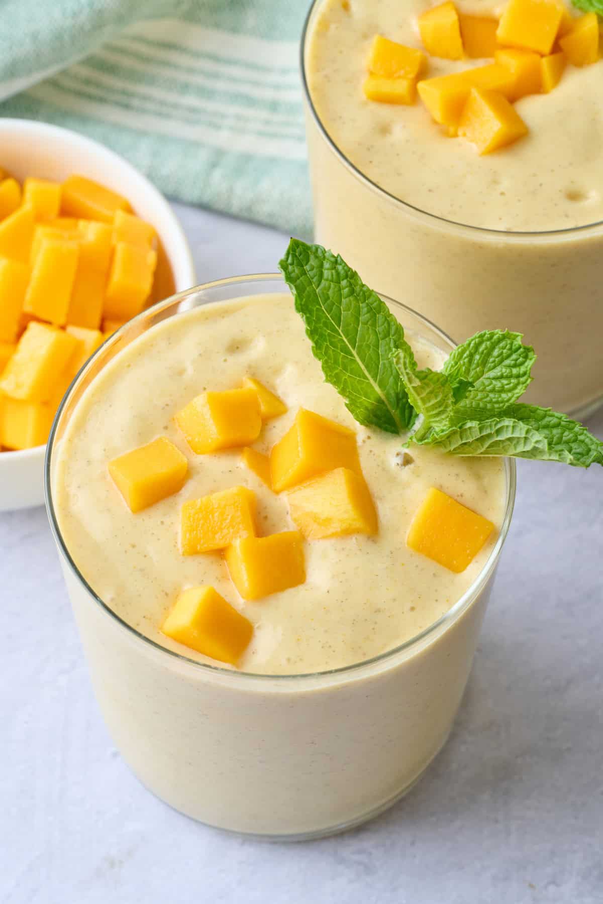 Best mango smoothie in small glasses topped with extra diced mango and fresh mint.