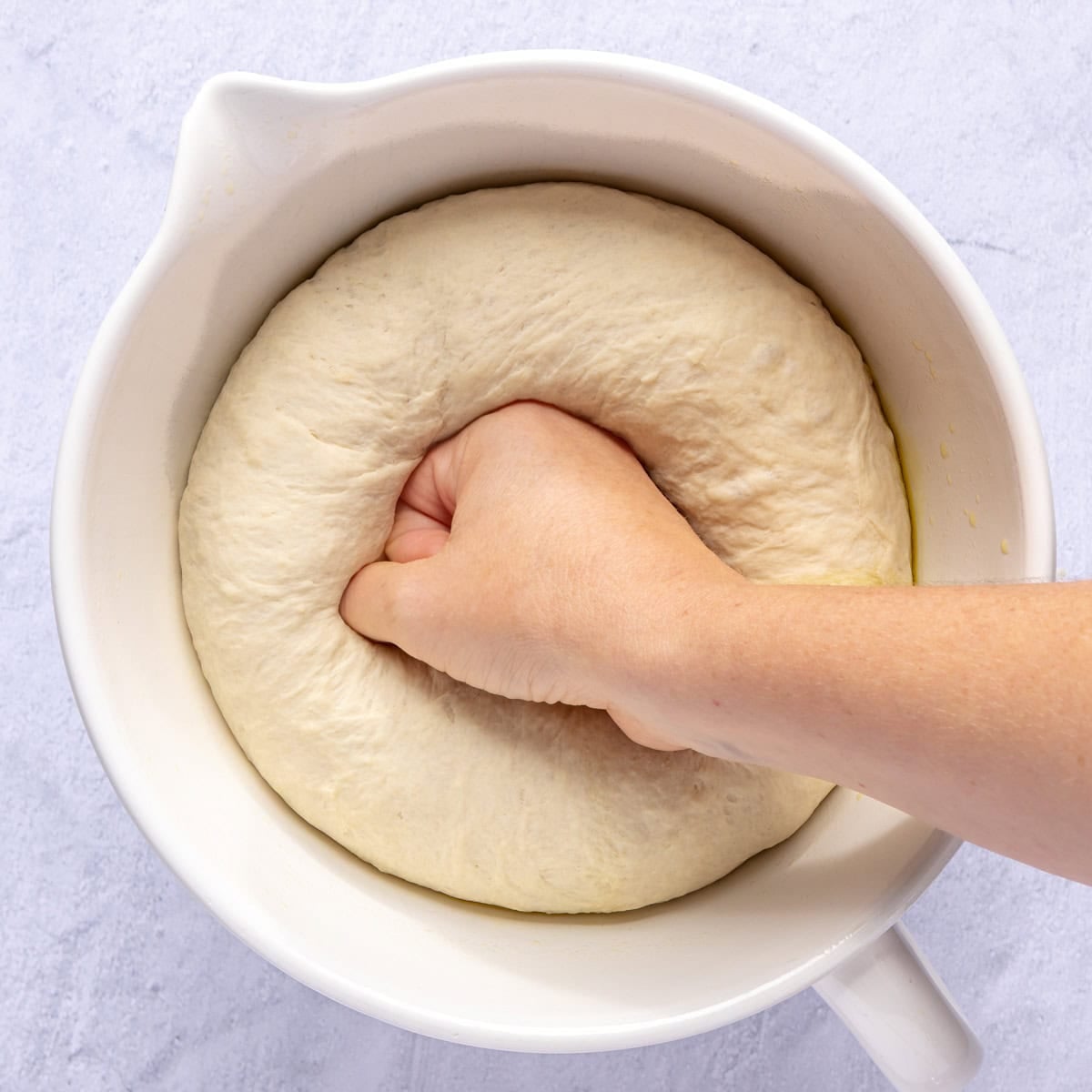 Hand punching down dough ball in bowl.