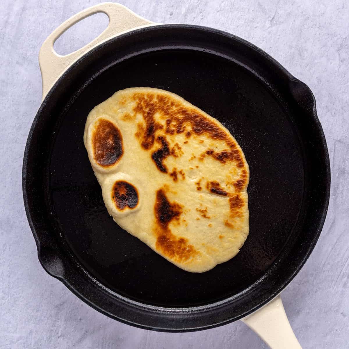 After flipping to show deeply golden brown naan with bubbled surface.
