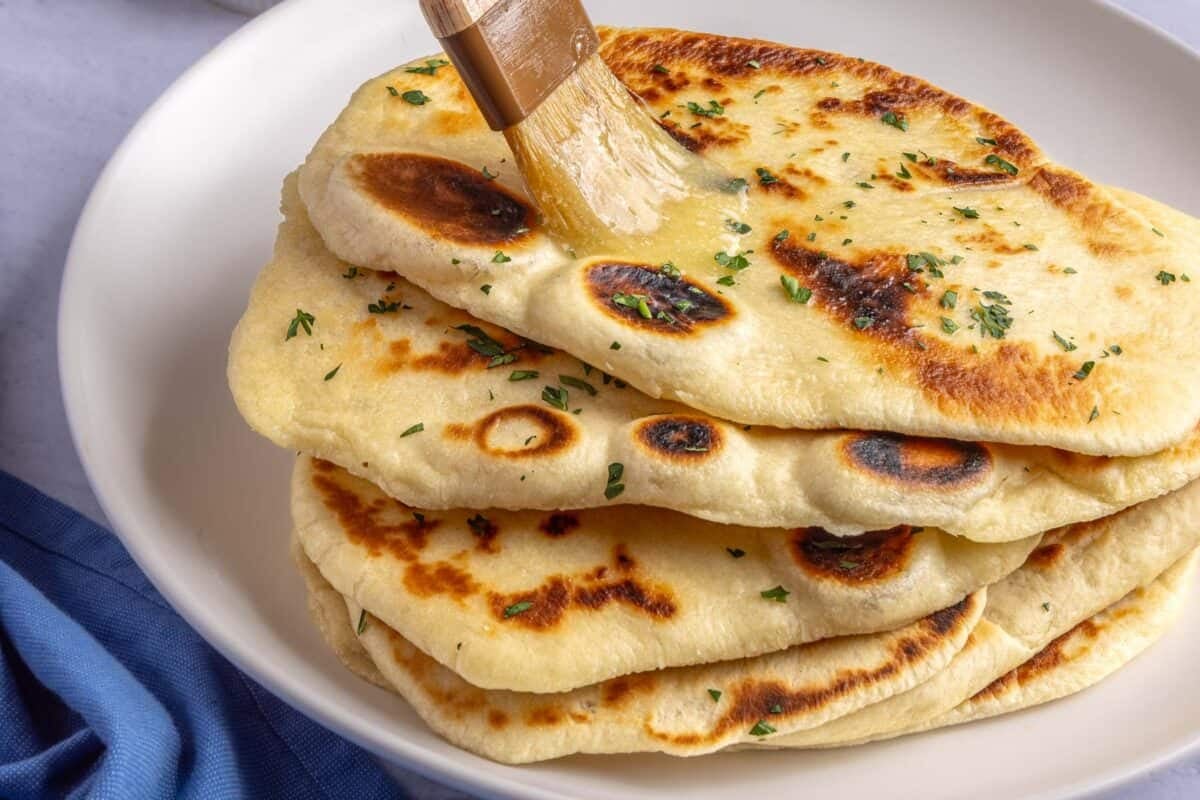 Butter being brushed on top of a stack of freshly cooked homemade naan.