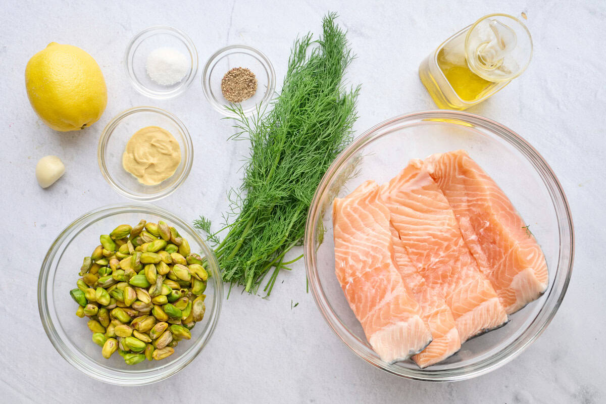 Ingredients for recipe: lemon, garlic, Dijon mustard, salt, pepper, shelled pistachios, fresh dill, salmon filets, and oil.