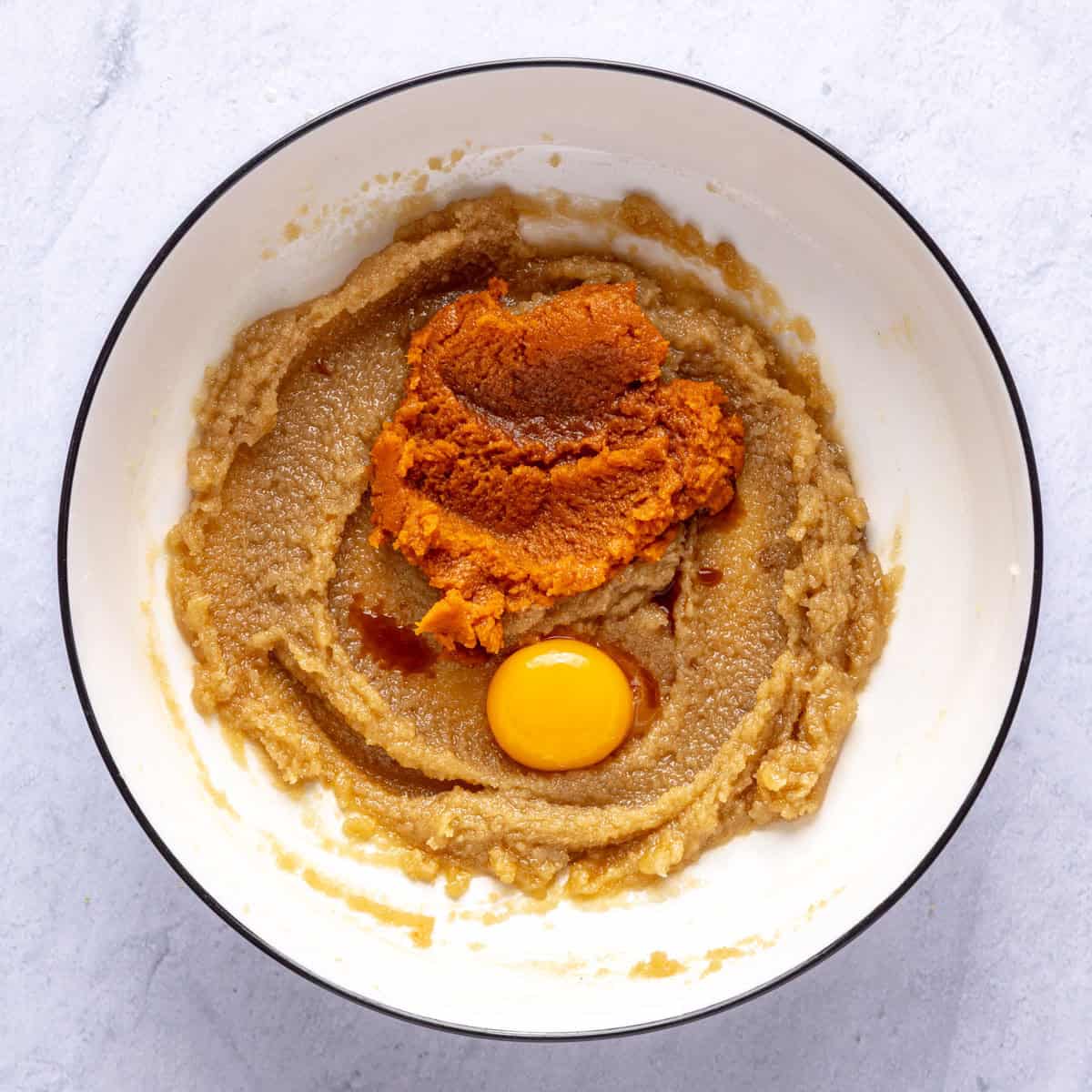 Butter sugar mixture in a bowl with pumpkin puree, an egg yolk and vanilla extract added.