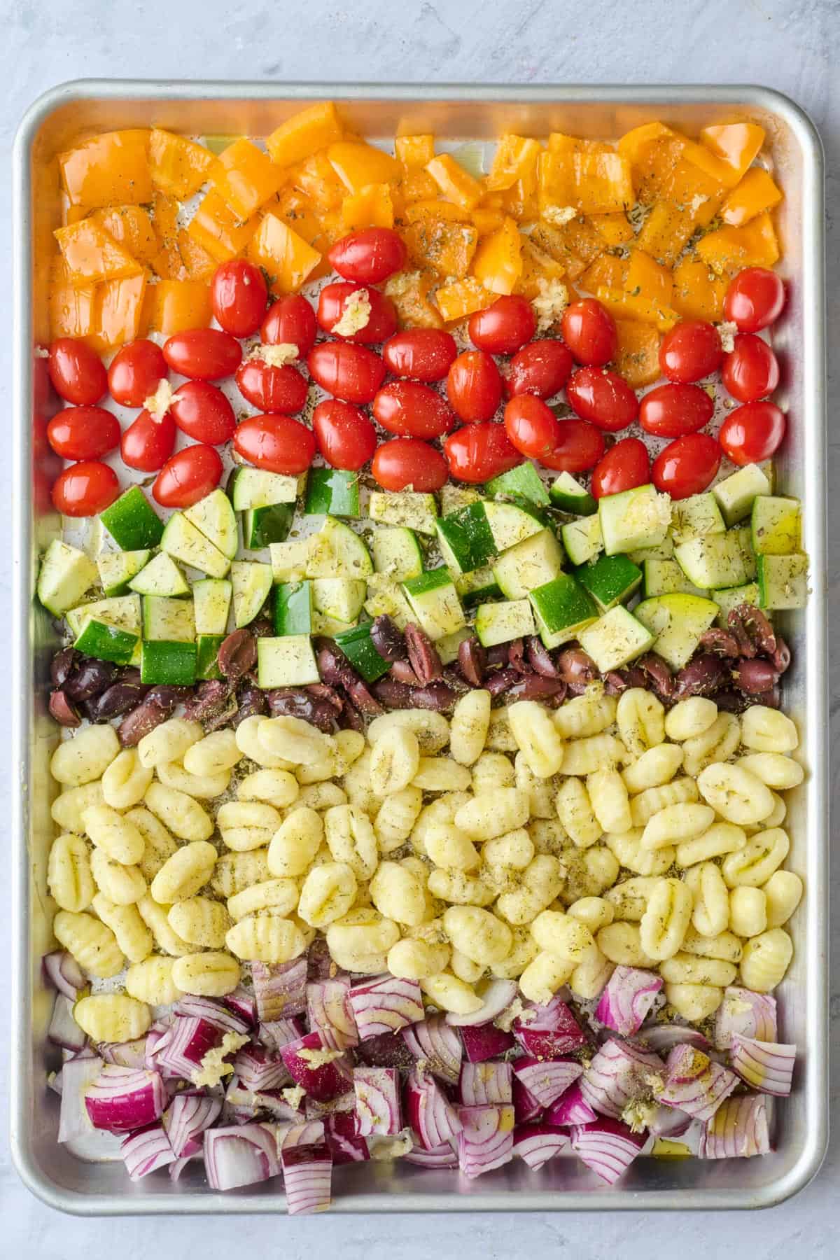 Gnocchi and veggies on a rimmed sheet pan with oil drizzled on top and sprinkled with the garlic and seasonings, before tossing.