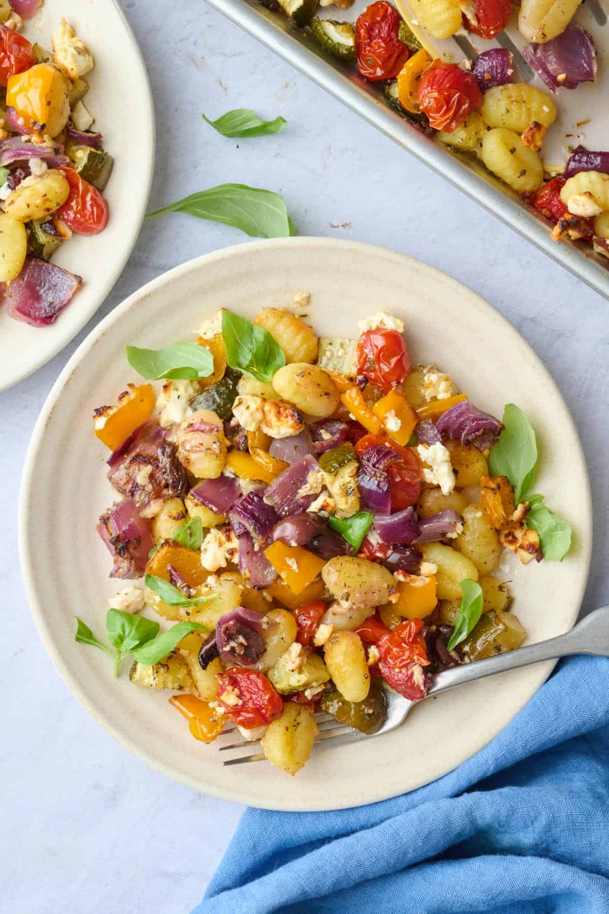 Serving of sheet pan gnocchi, roasted vegetables, and feta cheese, pan nearby.