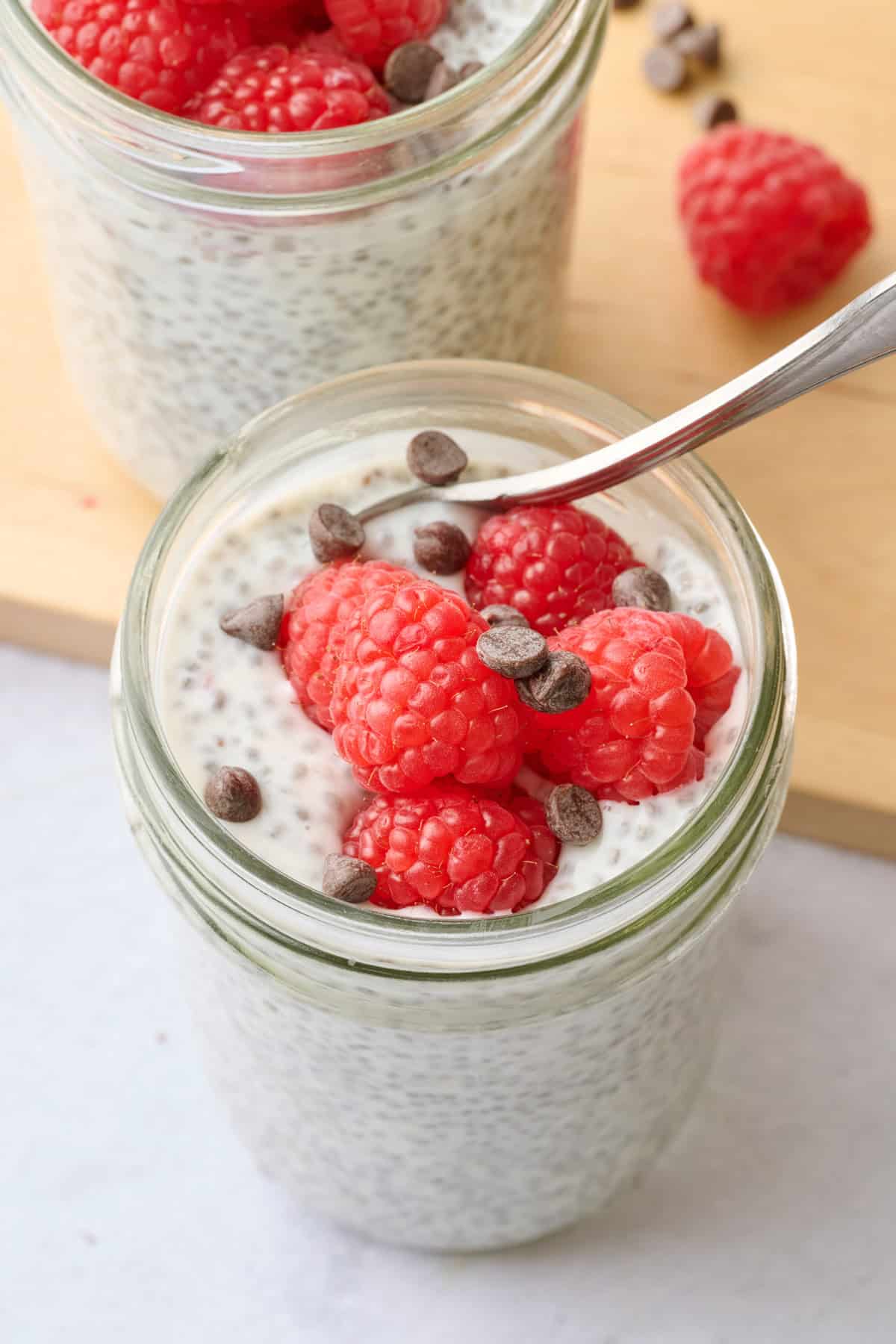 Yogurt chia pudding in a jar topped with fresh raspberries and chocolate chips.
