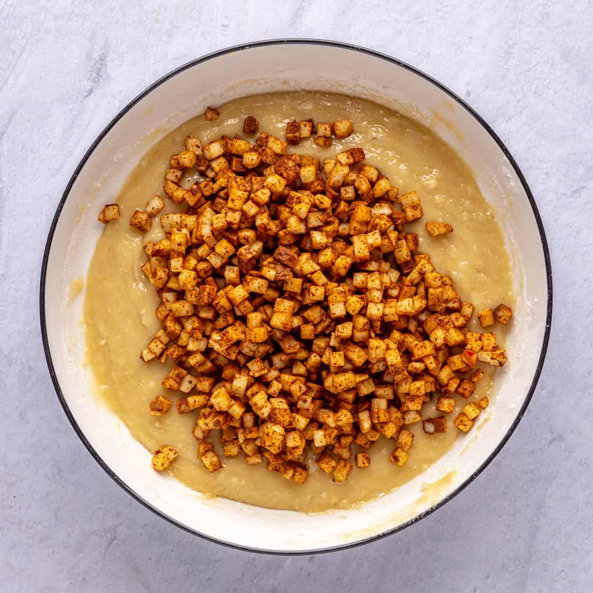 Batter for apple bread recipe in a bowl with cinnamon coated diced apples added on top before folding together.