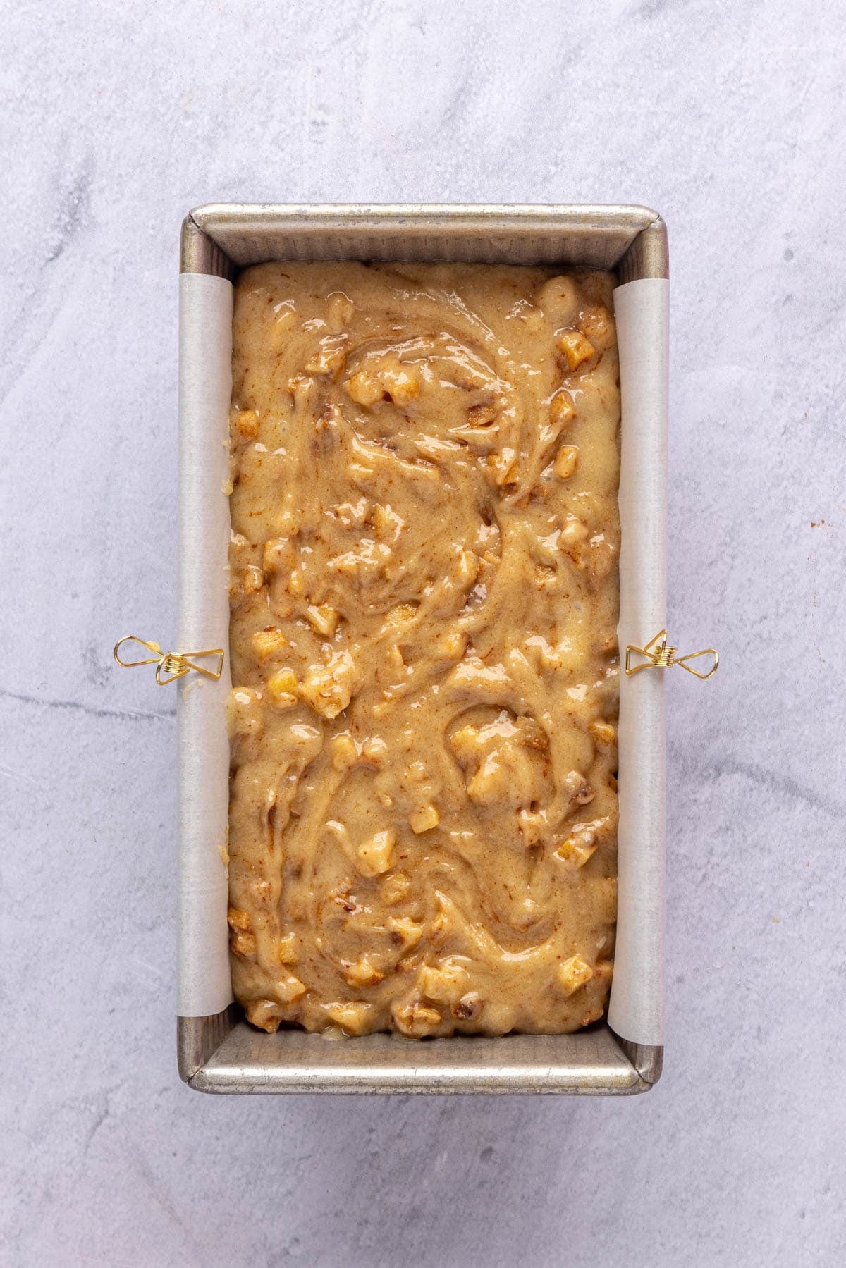 Loaf pan lined with parchment paper and filled with apple bread batter before baking.