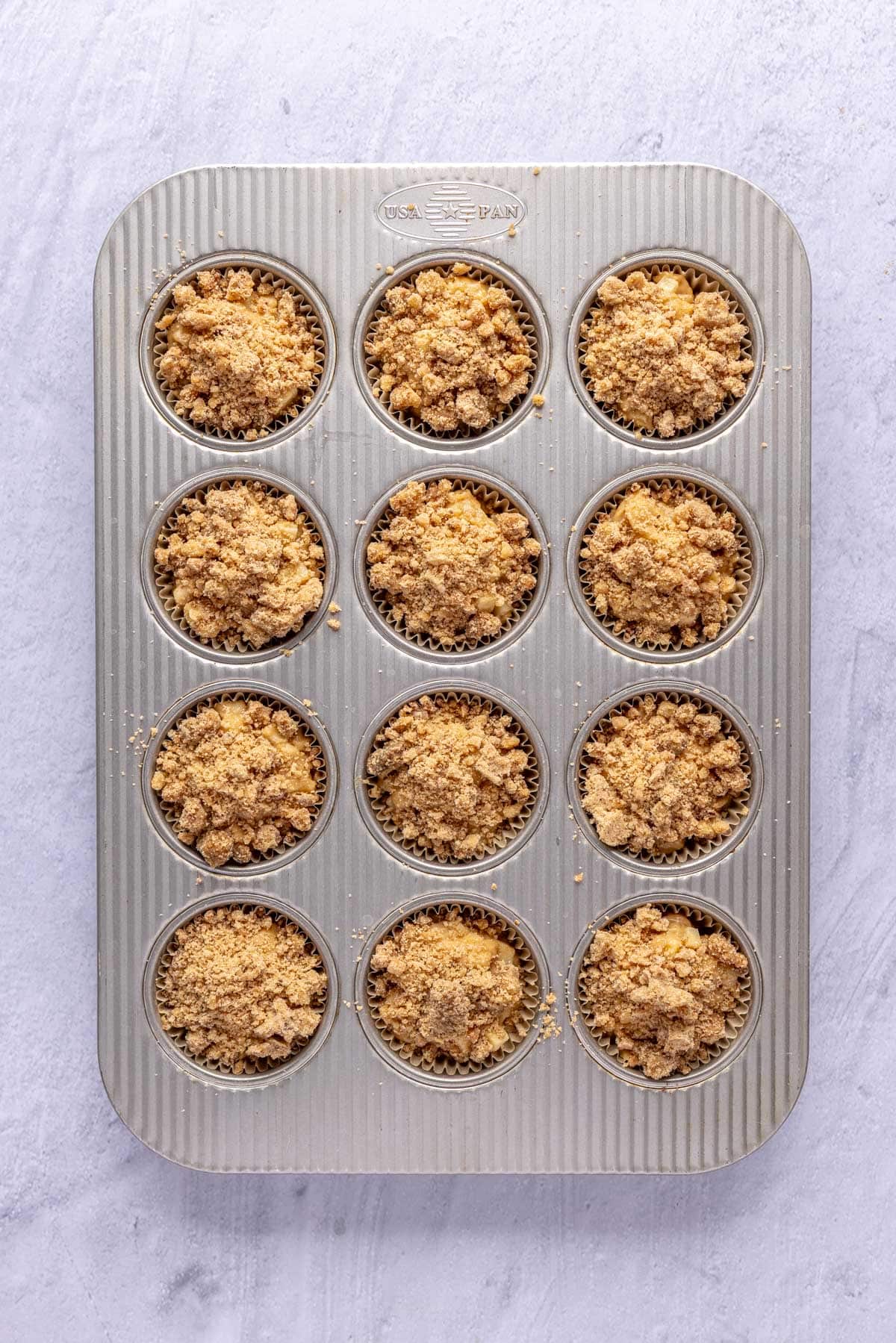 Muffin batter divided evenly into cupcake pan lined with parchment paper liners and crumble added on top.