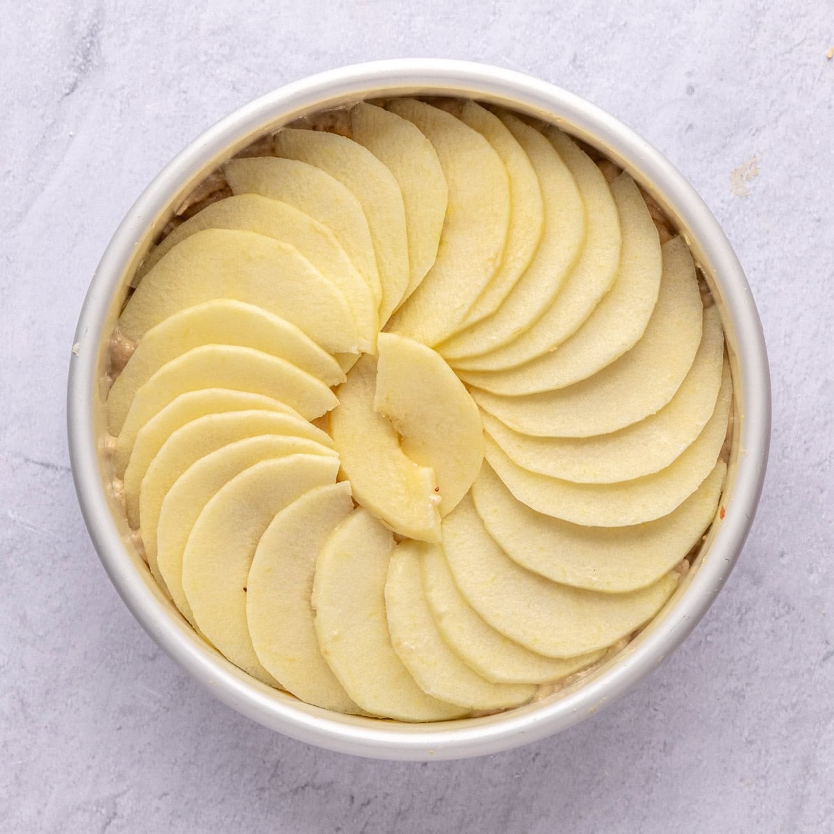 Cake batter for recipe in a cake pan with apple slices on top before baking.