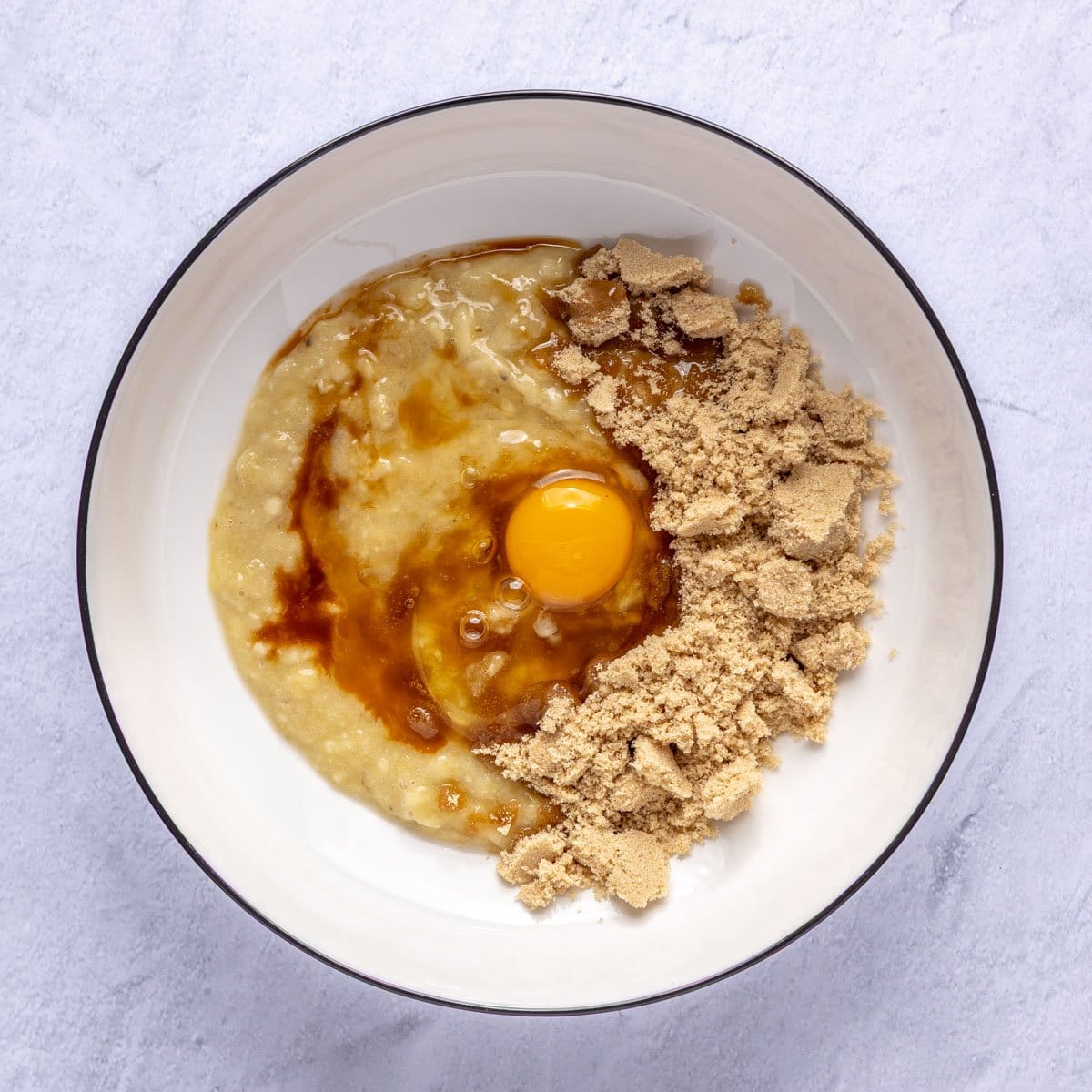 Mashed bananas in a bowl with brown sugar, egg and vanilla added.