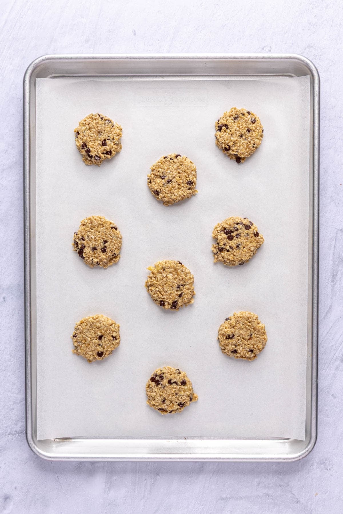 Cookie dough on a parchment lined baking sheet after flattening into ยฝ inch thickness.