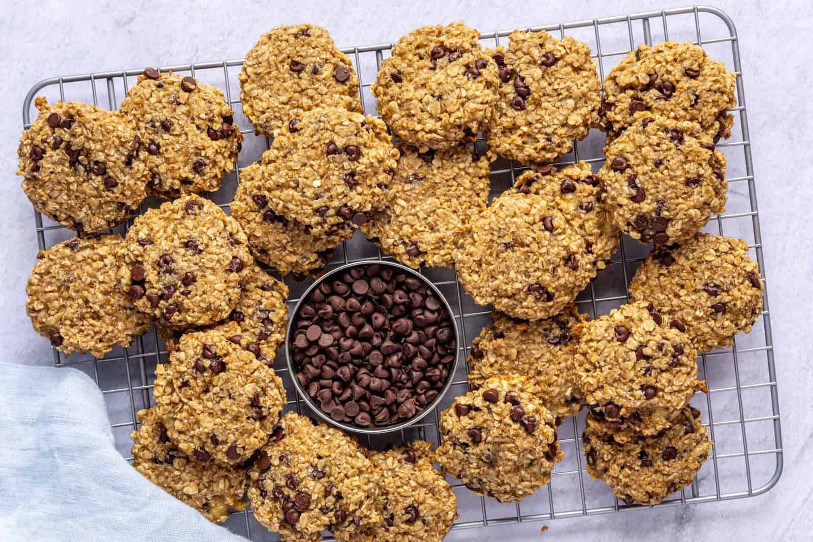 Banana oatmeal cookies on wire rack, small dish with chocolate chips.
