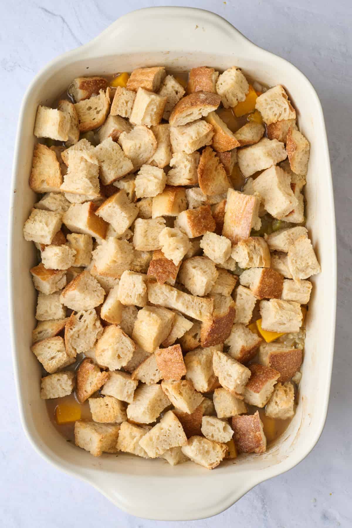 Toasted bread cubes and broth added to baking dish.