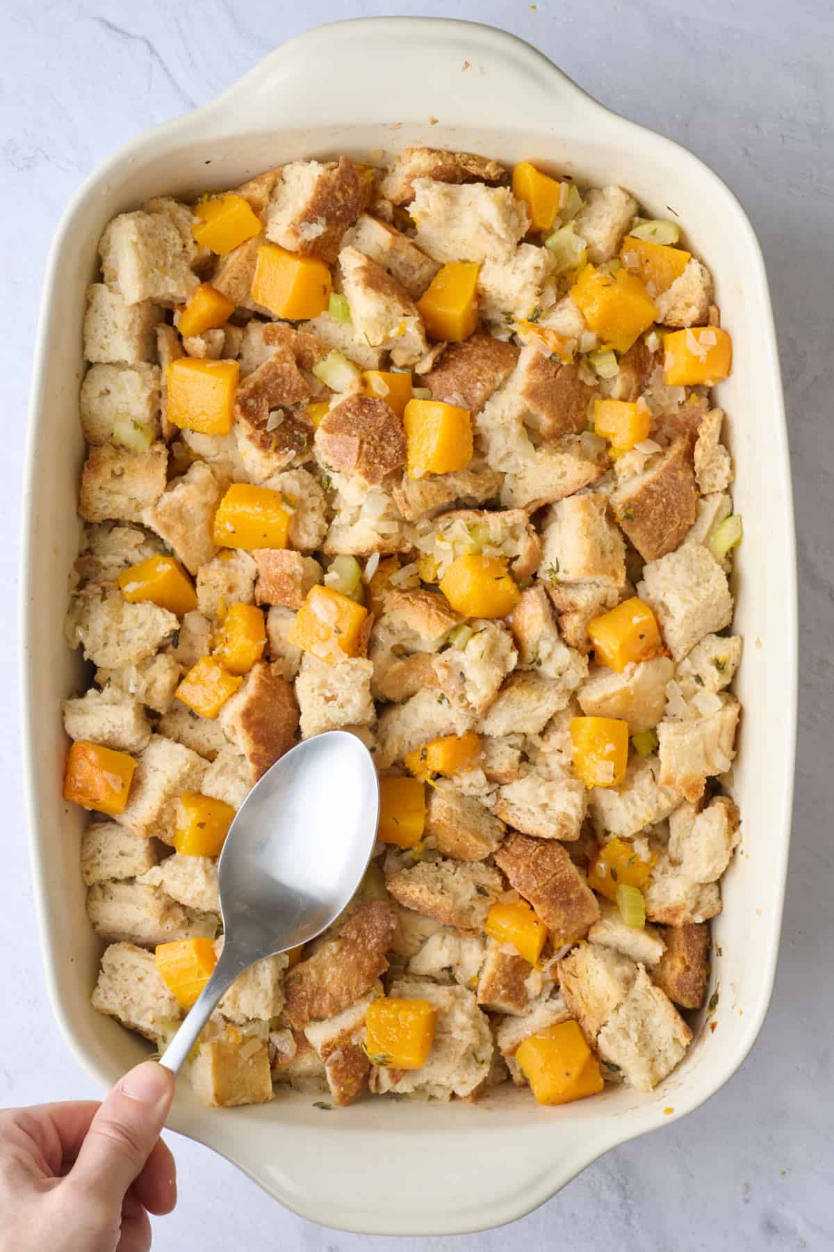 Spoon pressing stuffing into baking dish.