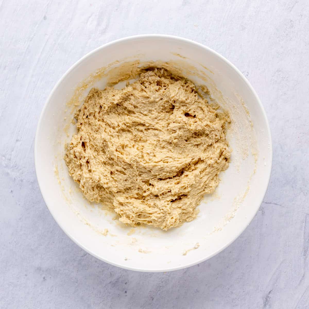 A bowl with a shaggy dough from combining the wet and dry ingredients for dinner roll recipe.