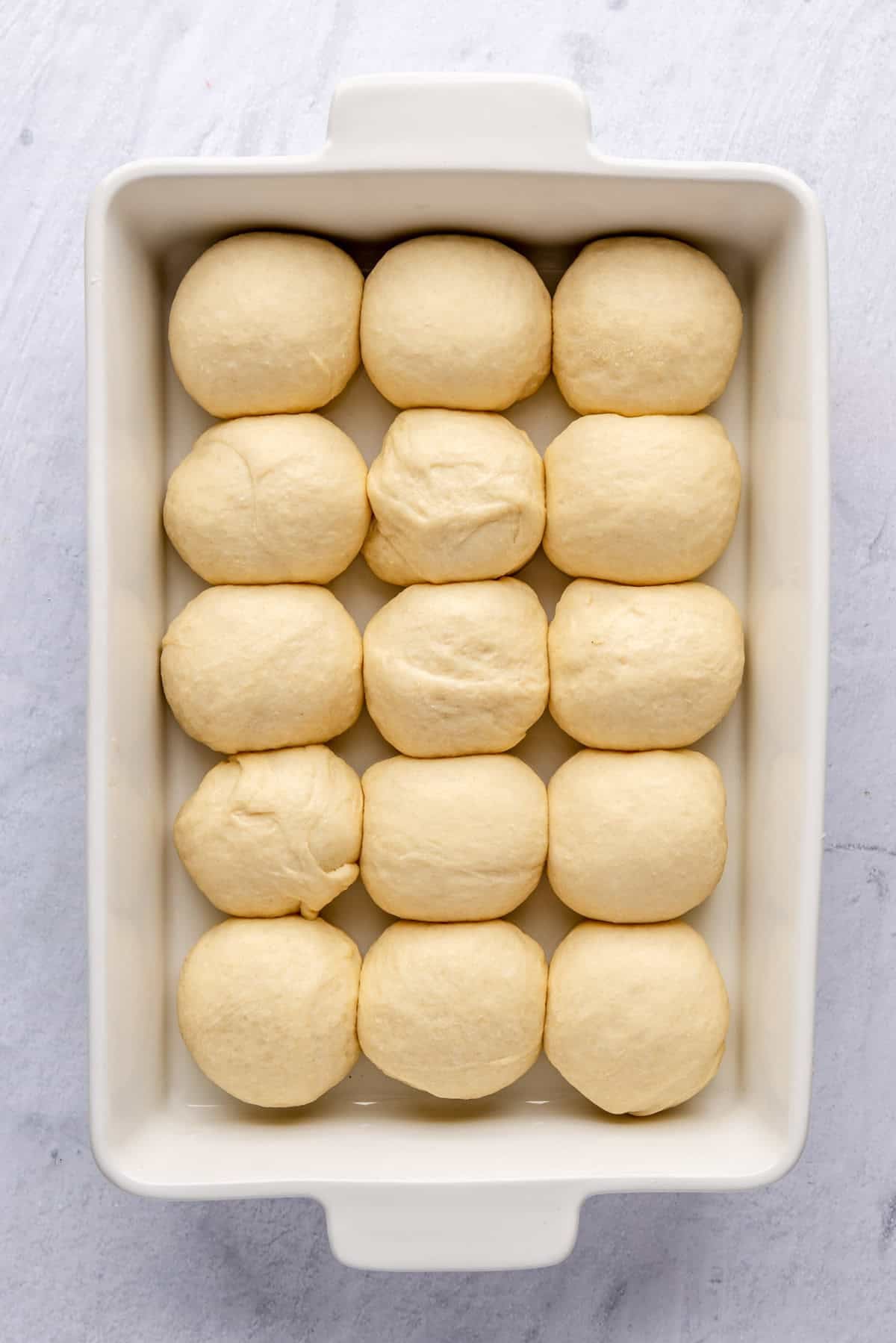 Puffed dough balls for dinner roll recipe in a baking dish after final rise before baking.