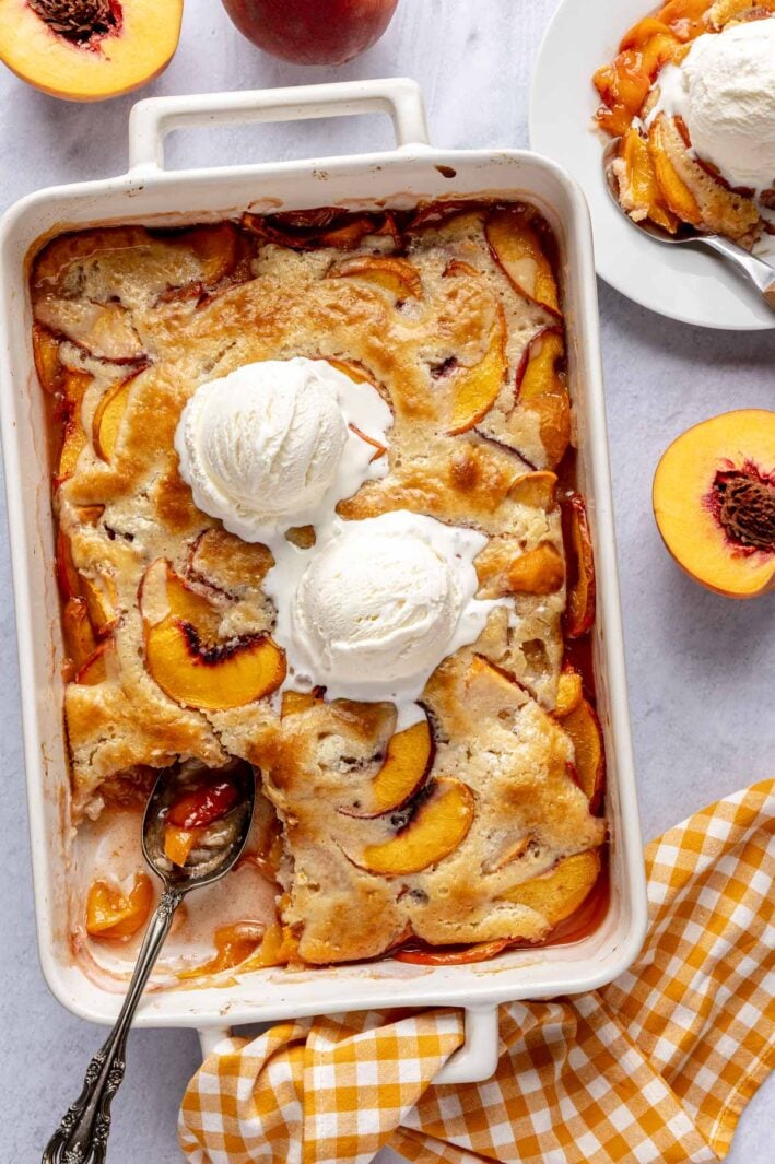 Homemade peach cobbler in baking dish with ice cream on top.