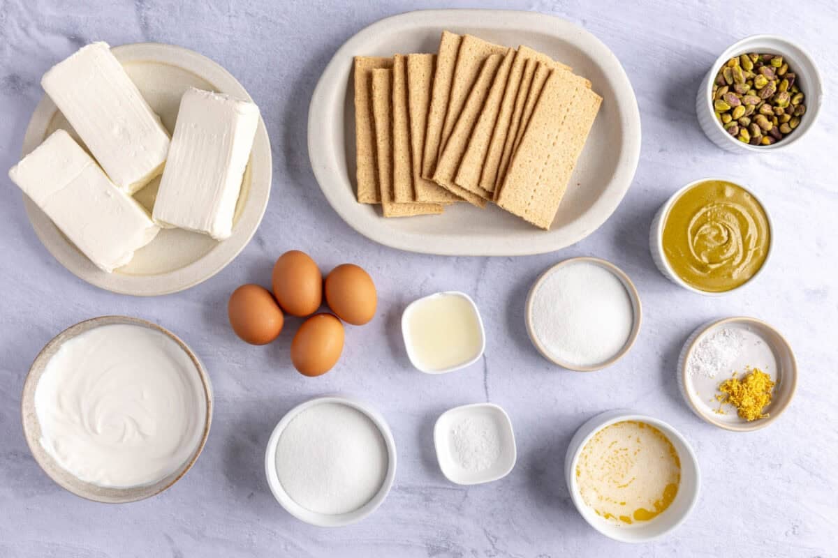 Ingredients for recipe: cream cheese, graham crackers, eggs, pistachios, pistachio butter, sour cream, sugar, salt, melted butter, lemon.