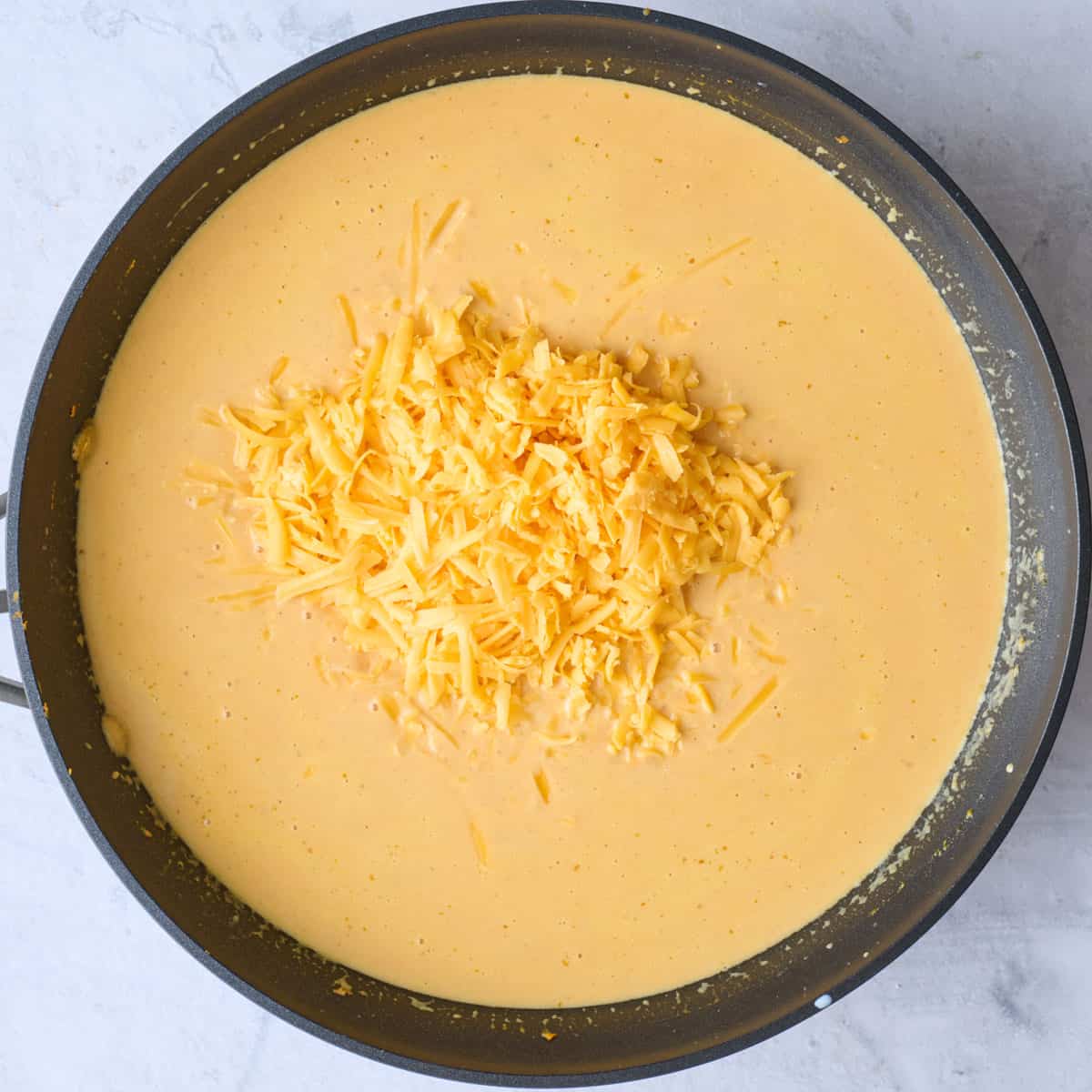 Shredded cheese added to sauce in skillet.
