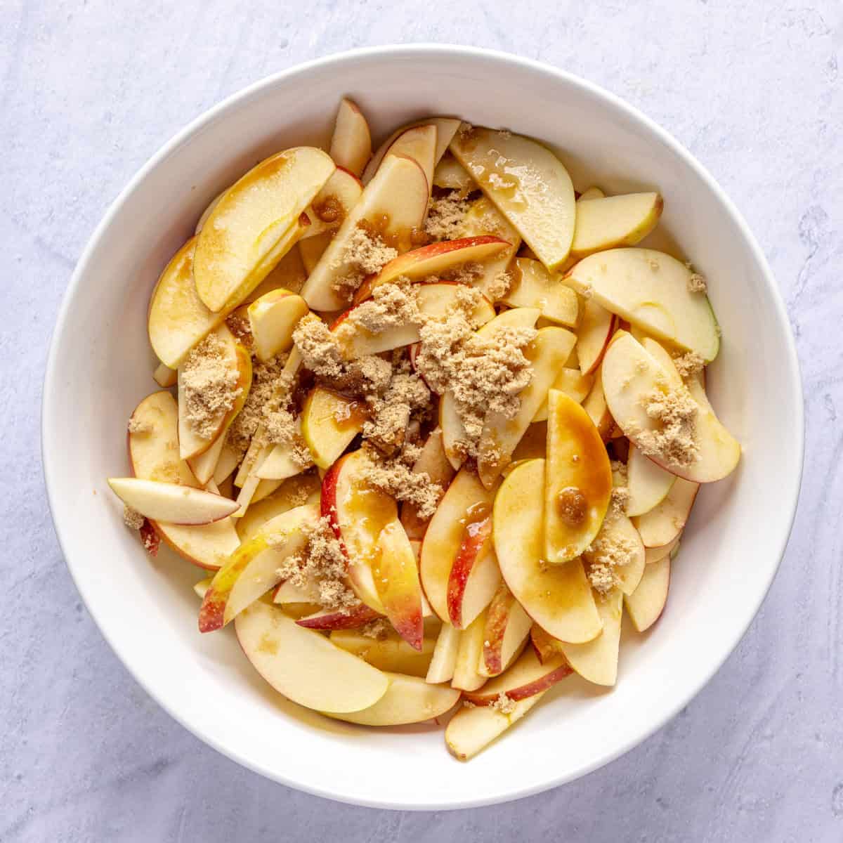 Apple slices, brown sugar, lemon juice and vanilla in a bowl before tossing together for apple tart filling.