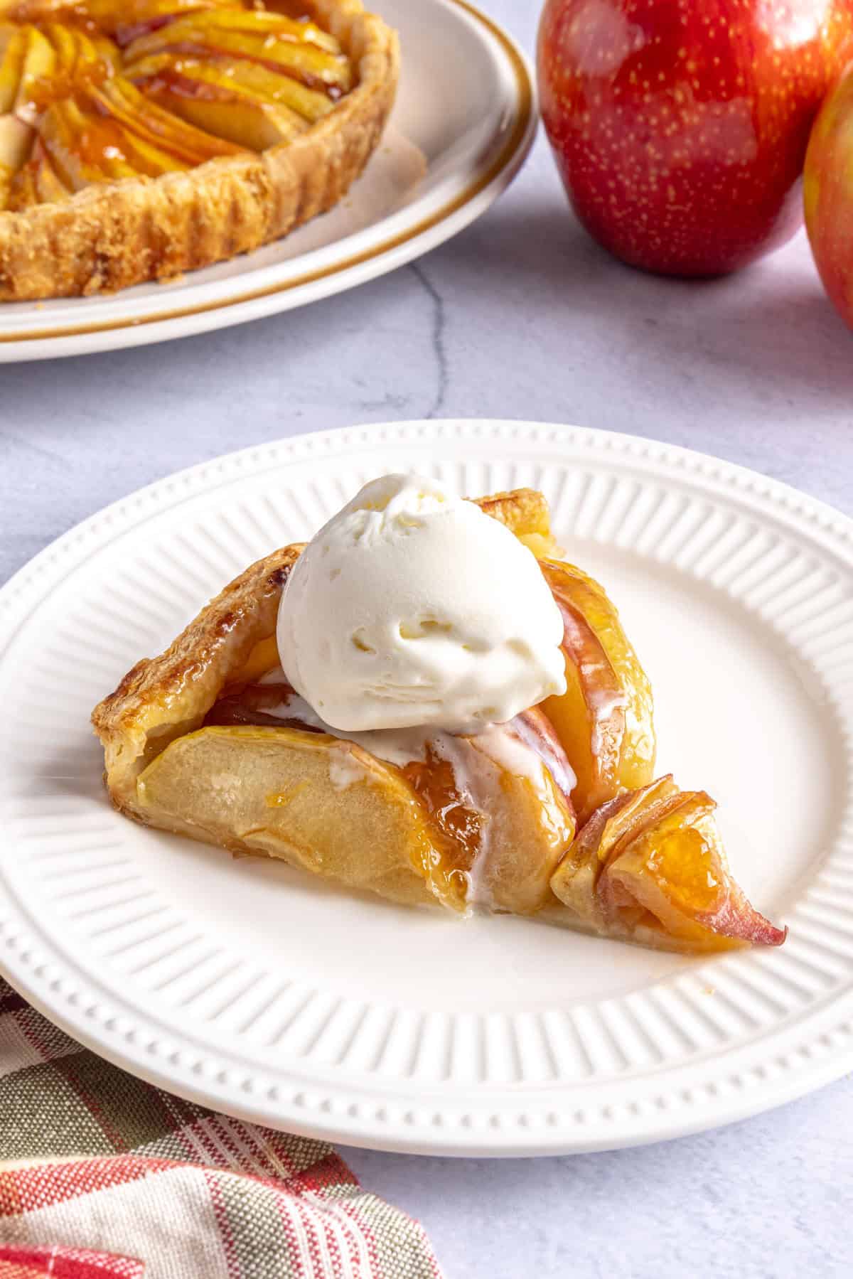 Slice of apple tart made using storebought puff pastry on a plate with a scoop of vanilla ice cream on top.