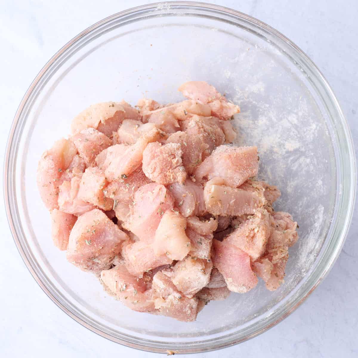 Chicken breast pieces in a bowl after tossing with seasonings and flour.