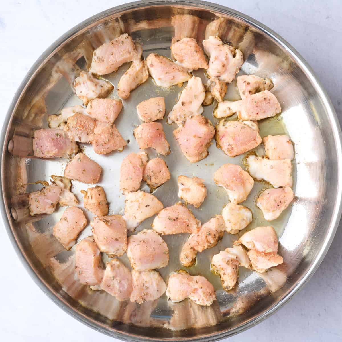 Seasoned chicken pieces in a hot oiled stainless steel pan.