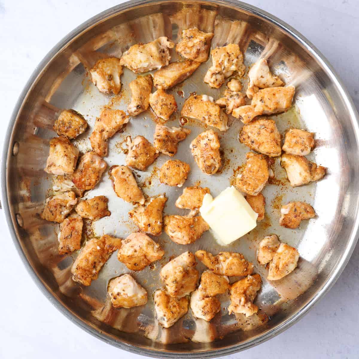 Chicken breast bites after cooking in a skillet with butter added to create a sauce.