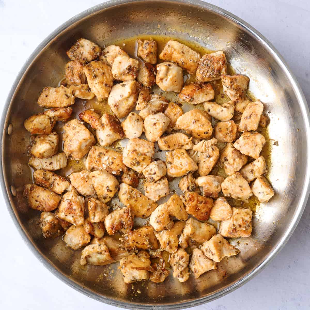 Chicken bites in a savory sauce after cooking in a skillet.