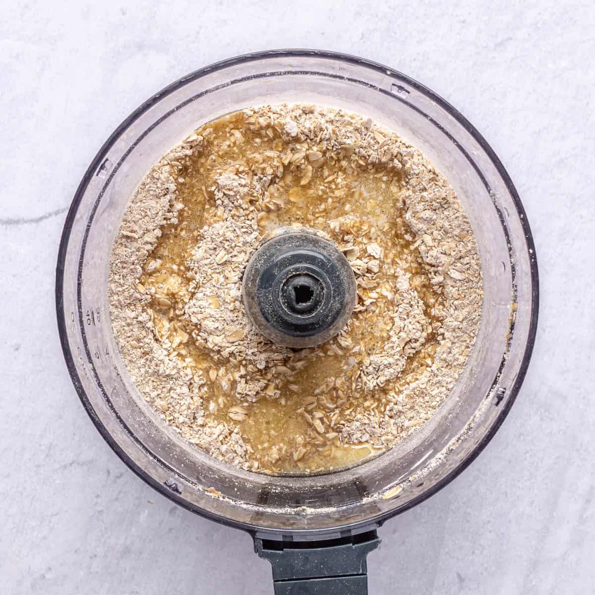 Rolled oats, sugar, salt and melted butter in the bowl of a food processor before processing for cheesecake crust.