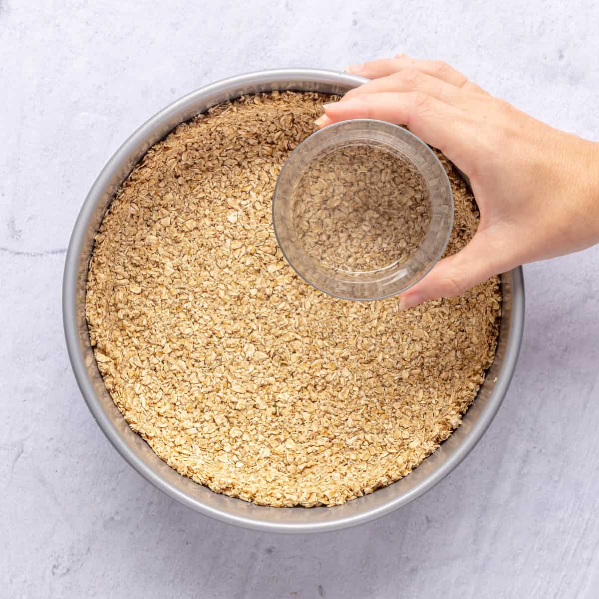 Oat crust mixture being pressed into a springform pan.