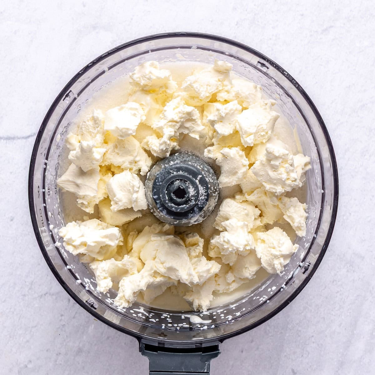 Cottage cheese after processing in a food processor with pieces of softened cream cheese and sugar added on top.