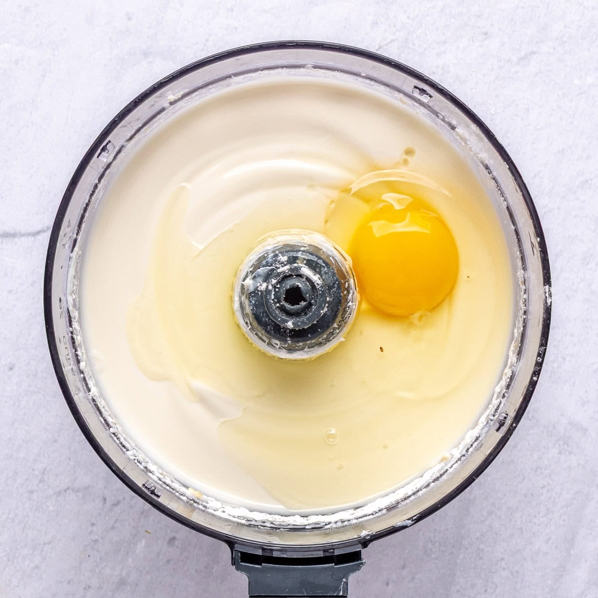 Cheesecake batter in a food processor with 1 egg added before mixing.