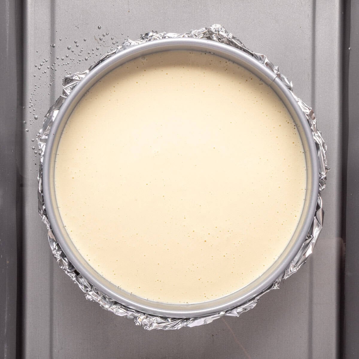 Final cottage cheesecake batter in the springform pan with oat crust wrapped in foil and placed in a large pan with hot water before baking.