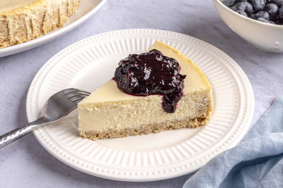 Slice of homemade cottage cheesecake with an oat crust and topped with blueberry compote.