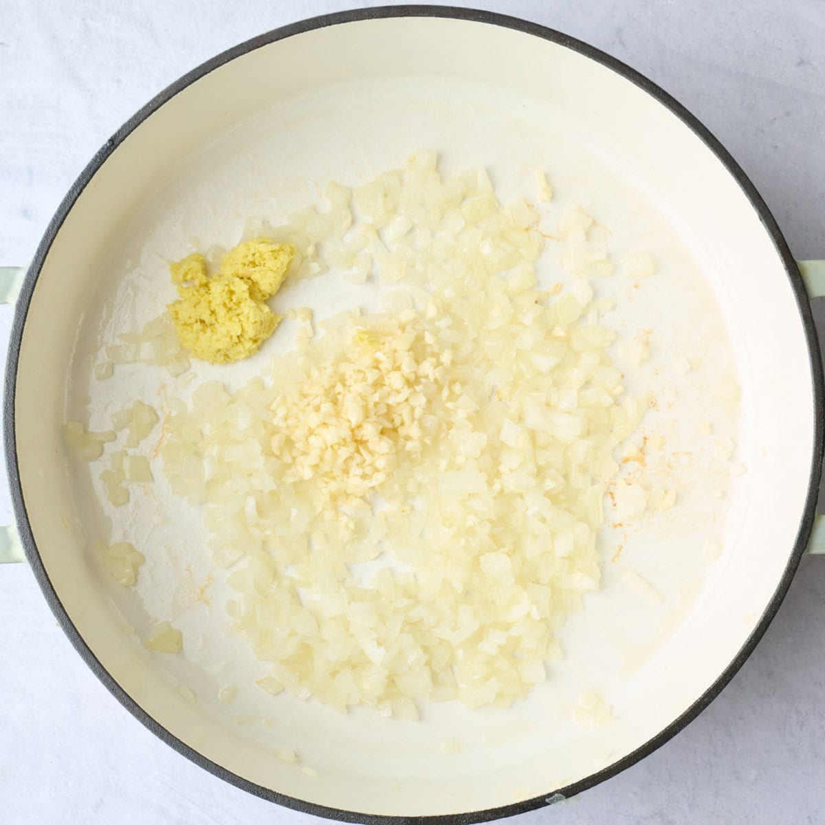 Cooked diced onions in a pot with grated ginger and garlic added for soup recipe.