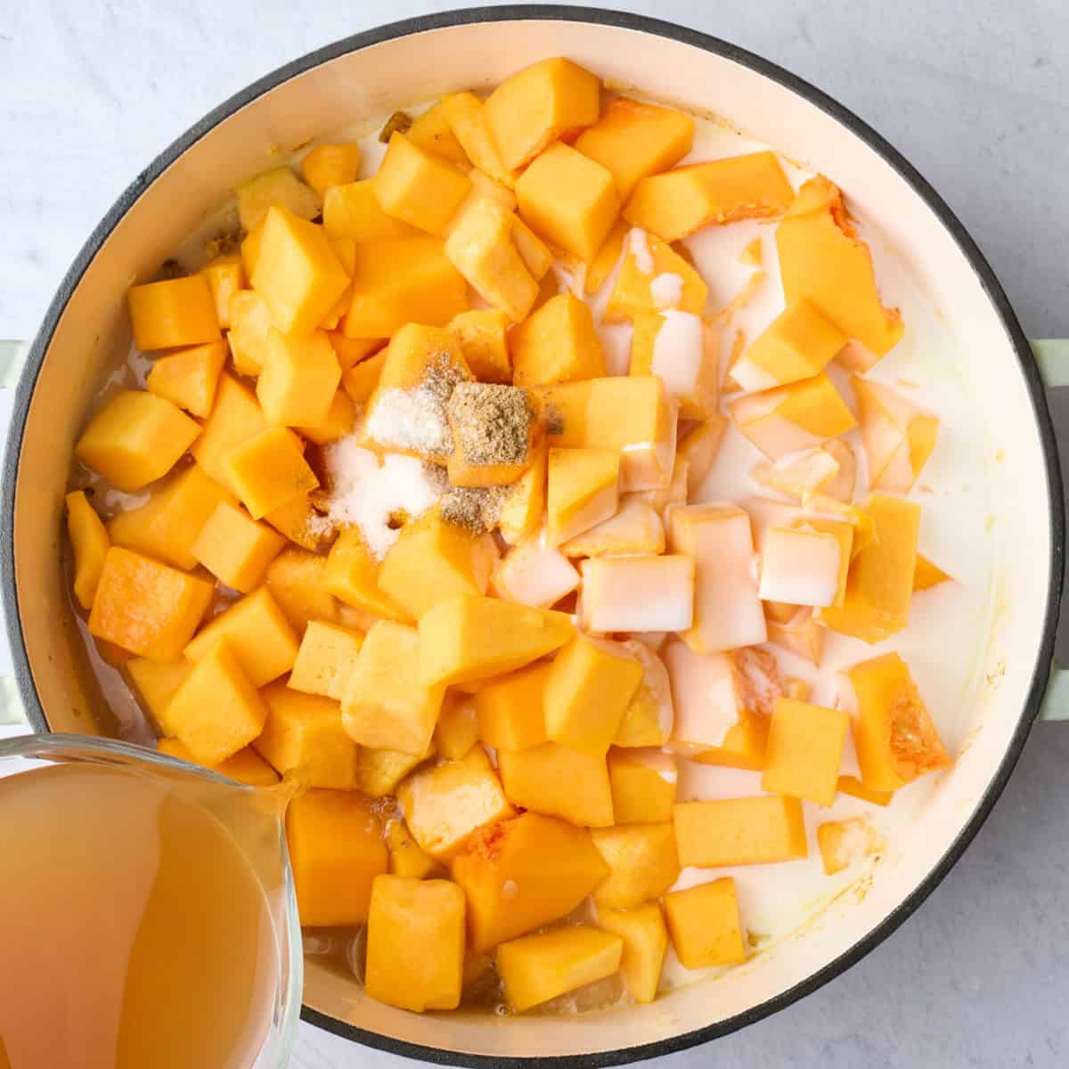 Cubed squash, remaining seasonings, and coconut milk added to the soup pot with broth being poured in.