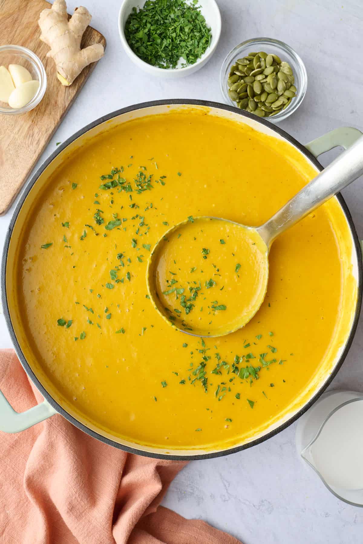 Curried butternut squash soup with coconut milk in a pot with a ladle lifting some up.