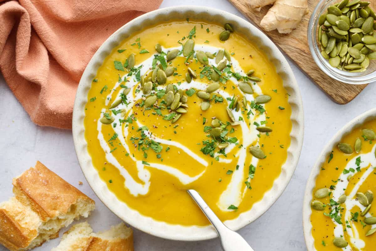 Easy curried butternut squash soup recipe served in a bowl with extra coconut milk, pepitas, and chopped parsley on top.