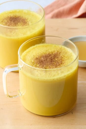 Warm spiced Golden Milk turmeric latte recipe in glass mugs with cinnamon sprinkled on top.